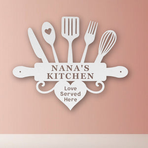 Decorative sign with kitchen utensils and 'Nana's Kitchen Love Served Here' text on a pink background