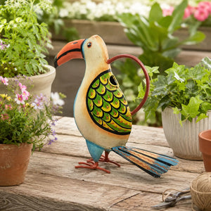 Decorative toucan-shaped watering can on a wooden surface with plants in the background