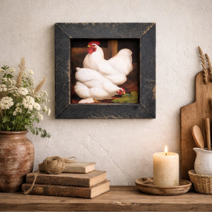 Framed artwork of chickens on a wall above a wooden table with decor items.