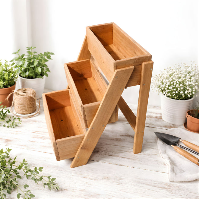 Wooden planter boxes on a wooden surface with plants and gardening tools.