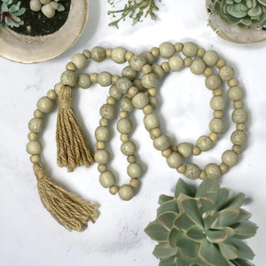 Decorative string of light-colored beads with tassels on a white surface with succulents.