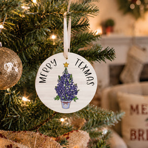 Merry Texmas bluebonnet Christmas ornament hanging on a lit Christmas tree in a cozy living room setting.