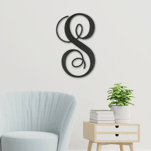 Decorative wall piece with a stylized letter 'S' on a light gray wall above a light blue chair and a small table with books and a plant.