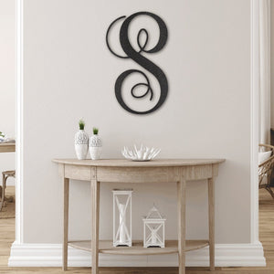 Wooden console table with decorative items against a white wall with a large letter 'S' sculpture.