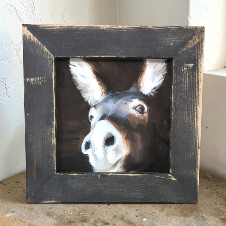 Framed painting of a donkey's face on a wooden surface.