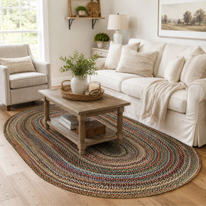 5 x 8 foot multicolor braided oval rug in a bright farmhouse living room with a white sofa, neutral armchair, rustic wood coffee table, and warm wood flooring.