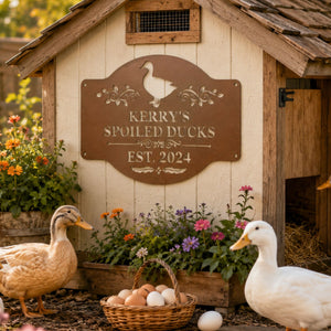 Copper personalized duck house sign with see-through cutout lettering mounted on a rustic cream duck coop, surrounded by white and buff egg-laying ducks, flowers, and a basket of fresh eggs.