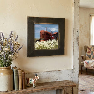 Framed artwork of a red tractor in a field on a wall above a wooden bench with decor items.