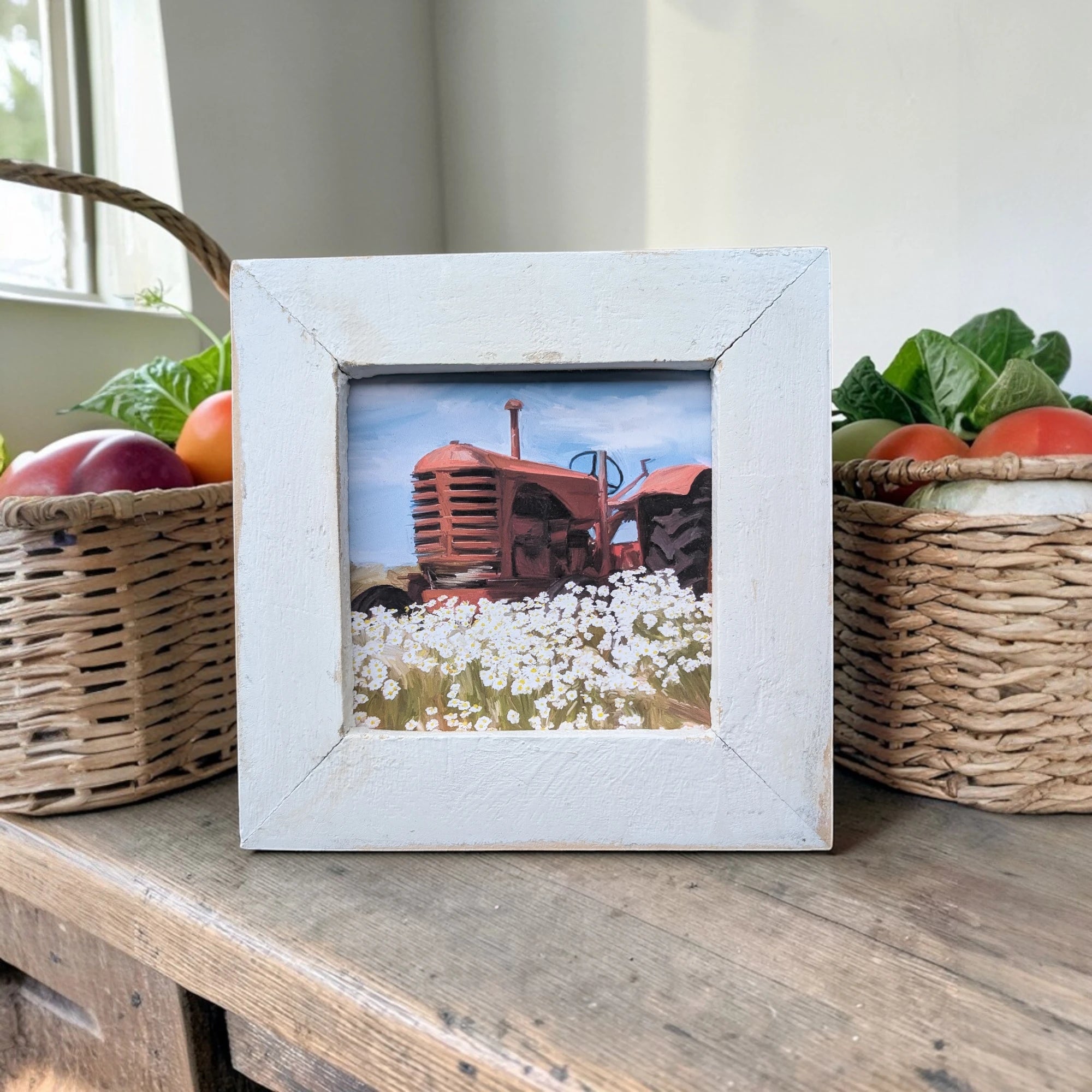 Framed picture of a red tractor in a field with baskets of apples and vegetables on a wooden surface.