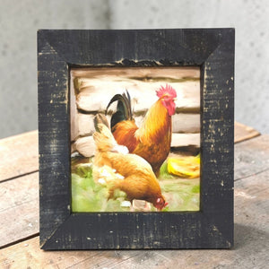 Framed picture of two chickens on a wooden surface with a gray background