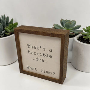 Wooden sign with text 'That's a horrible idea. What time?' in front of potted succulents.
