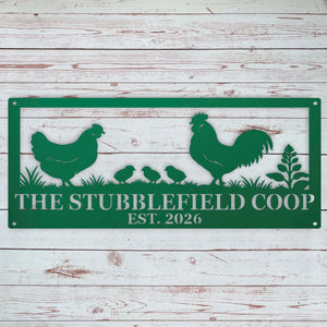 A green metal sign with a silhouette design of a rooster, hen, three chicks, and plants, with the text 'THE STUBBLEFIELD COOP EST. 2026' in white, displayed against a whitewashed wooden plank background.