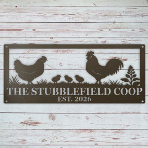 A rectangular metal sign with a silhouette design of a rooster, hen, three chicks, and a plant, with the text 'THE STUBBLEFIELD COOP EST. 2026' on a whitewashed wood plank background.