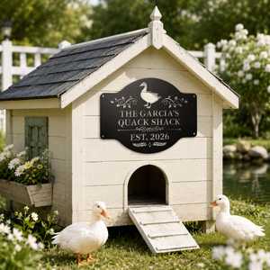 Custom black metal duck house sign displayed on a white wooden duck coop with white ducks, flowers, grass, and a garden pond.