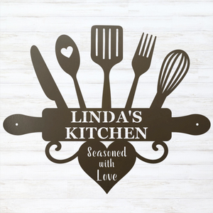 A dark brown metal kitchen-themed wall sign featuring silhouettes of kitchen utensils and a rolling pin with the text 'LINDA'S KITCHEN' and 'Seasoned with Love' on a white wood-plank background.