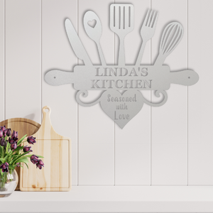 Decorative metal wall art with kitchen utensils and 'Mom's Kitchen Love Served Here' text on a white wooden panel background.