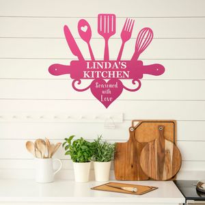 A pink kitchen-themed wall decal reading 'LINDA'S KITCHEN' and 'Seasoned with Love' is displayed on a white shiplap wall above a kitchen counter with wooden cutting boards, potted herbs, and utensils.