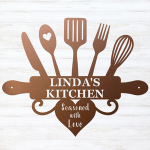 A decorative metal kitchen sign featuring silhouettes of cooking utensils and a rolling pin with the text 'LINDA'S KITCHEN' and 'Seasoned with Love' in white, shown on a white wood-plank background.